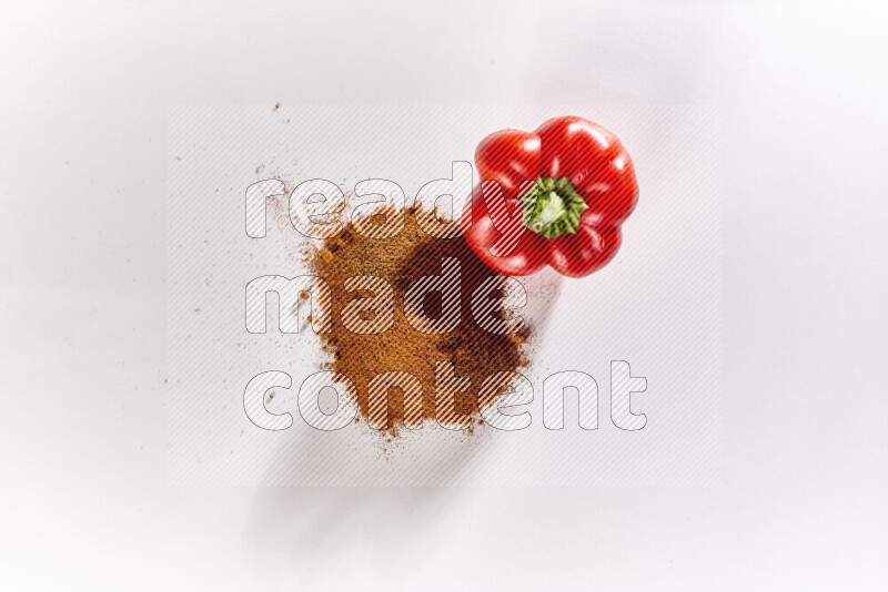 A bunch of ground paprika powder with a red bell pepper beside it on white background