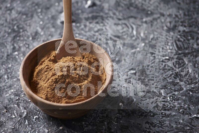 Wooden bowl full of cinnamon powder with a wooden spoon on a textured black background in different angles