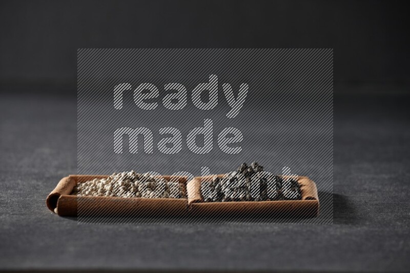 مربعان من أعواد القرفة ممتلئان بحبوب الفلفل الأبيض وحبوب الفلفل الأسود علي خلفية سوداء