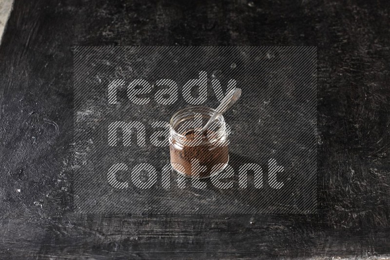 وعاء زجاجي ممتلئ ببودرة القرنفل مع ملعقة معدنية على أرضية سوداء