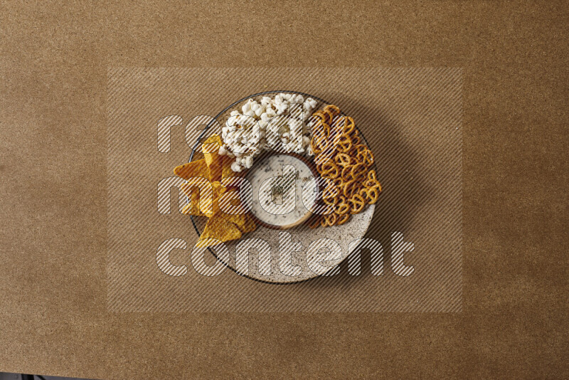 Assorted snacks on a pottery plate with a dipping on brown background