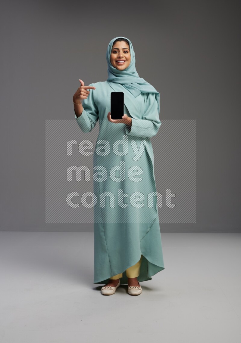 Saudi Woman wearing Abaya standing showing phone to camera on Gray background