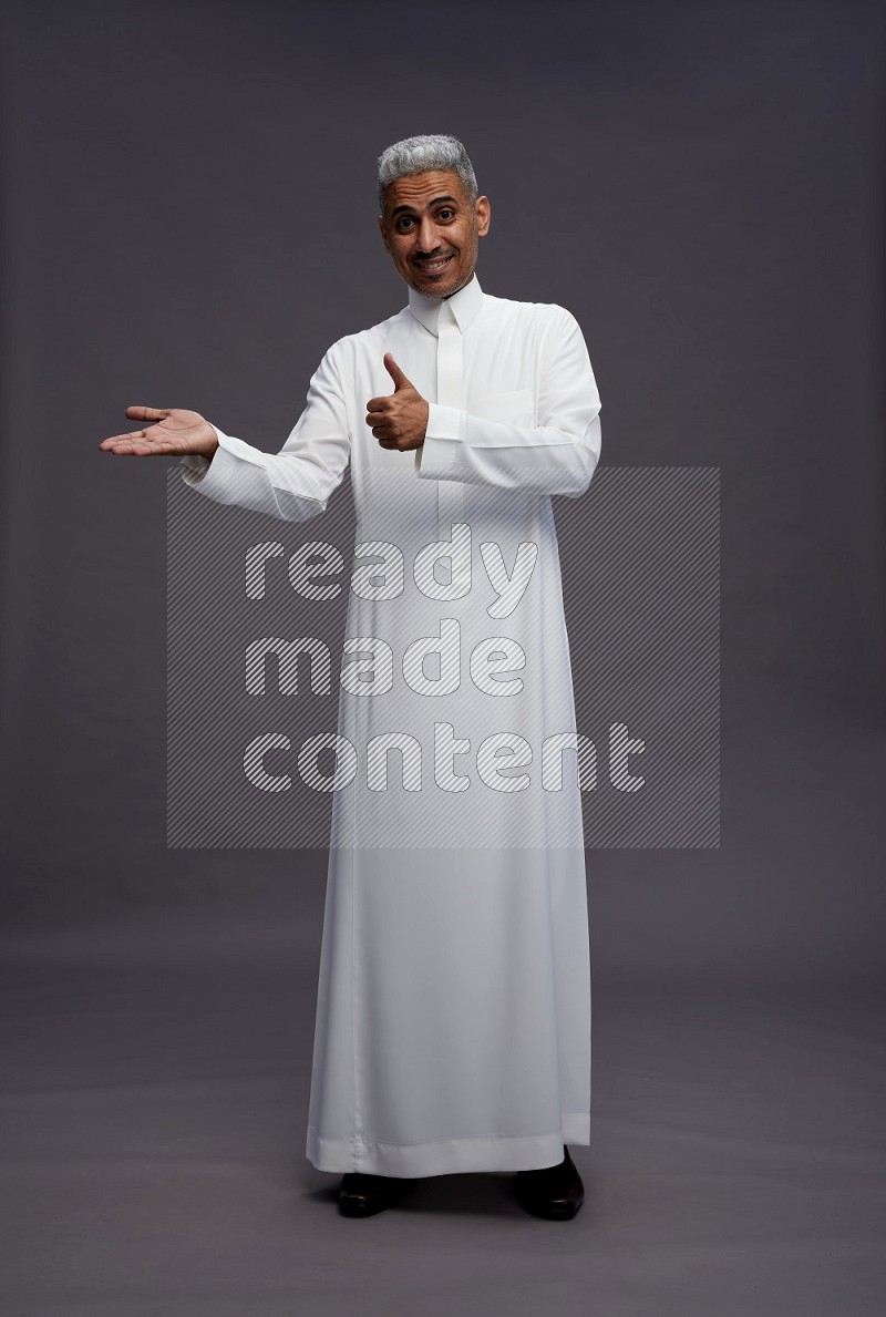 Saudi man wearing thob standing interacting with the camera on gray background