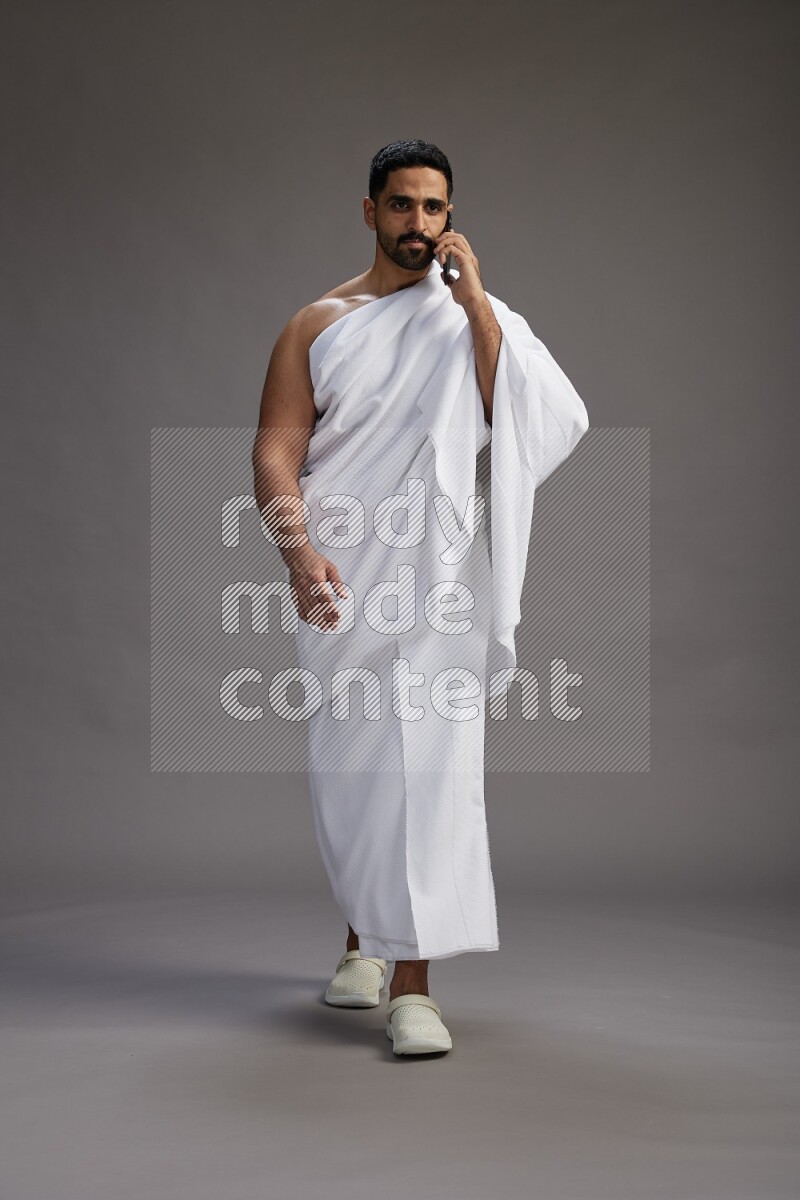A man wearing Ehram Standing talking on phone on gray background