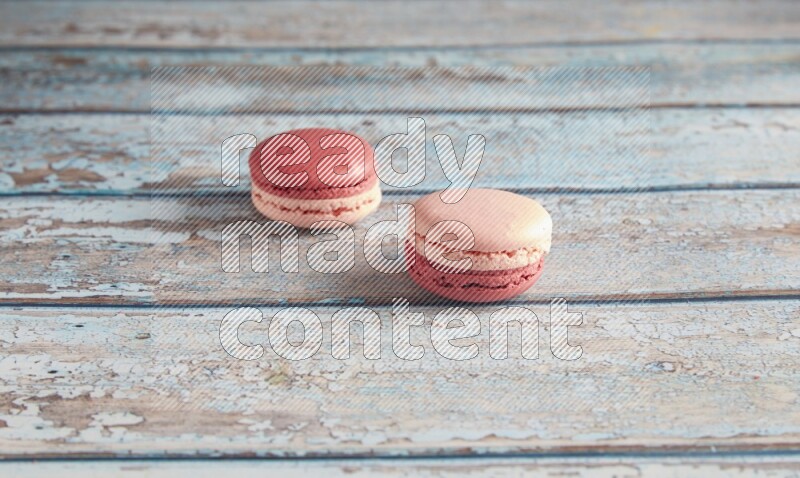 45º Shot of two Pink Litchi Raspberry macarons on light blue wooden background