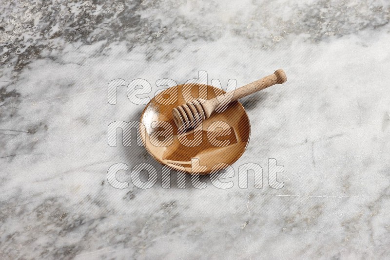 Multicolored Pottery Plate with wooden honey handle in it, on grey marble flooring, 65 degree angle