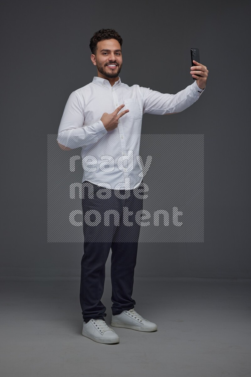 A man wearing smart casual and taking selfie with his phone eye level on a gray background
