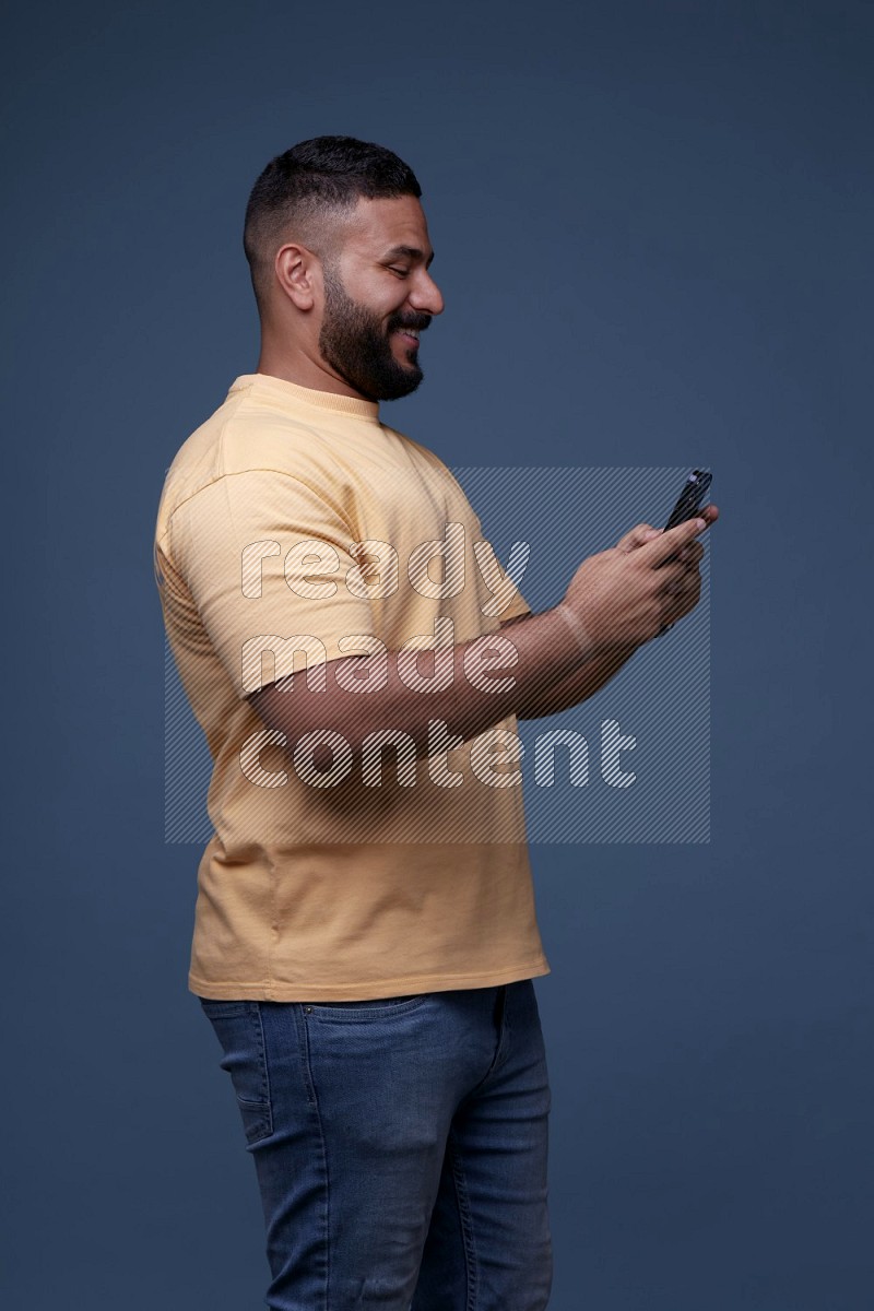 A man Texting on his phone on Blue Background wearing Orange T-shirt