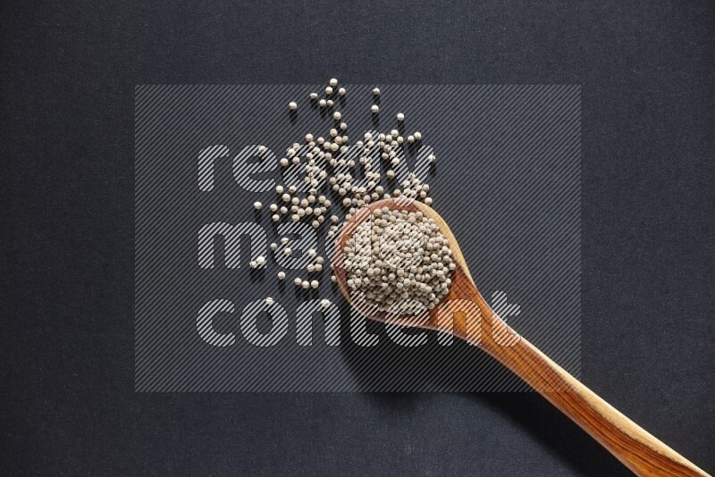 A wooden ladle full of white pepper beads on black flooring