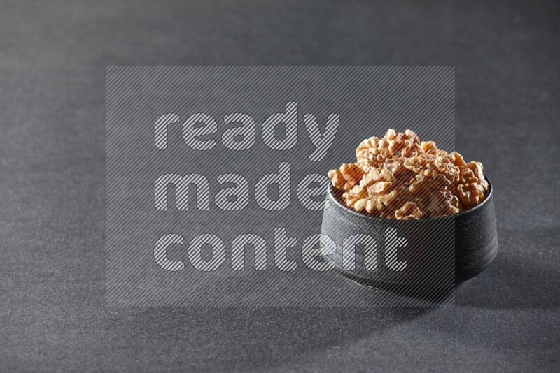 A black pottery bowl full of peeled walnuts on a black background in different angles