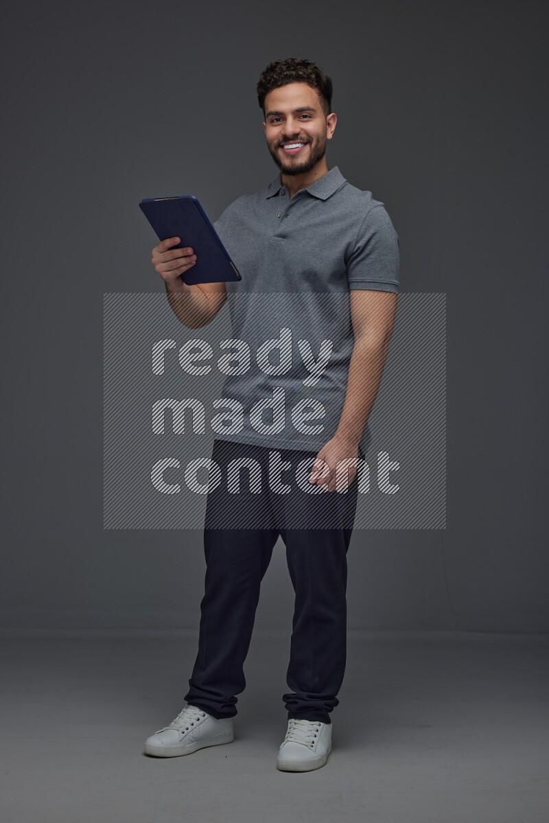 A man wearing casual standing and using his tablet and making multi hand gestures different angles eye level on a gray background