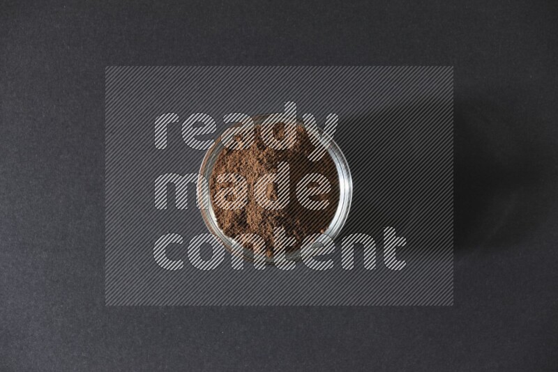 A glass bowl full of cloves powder on black flooring