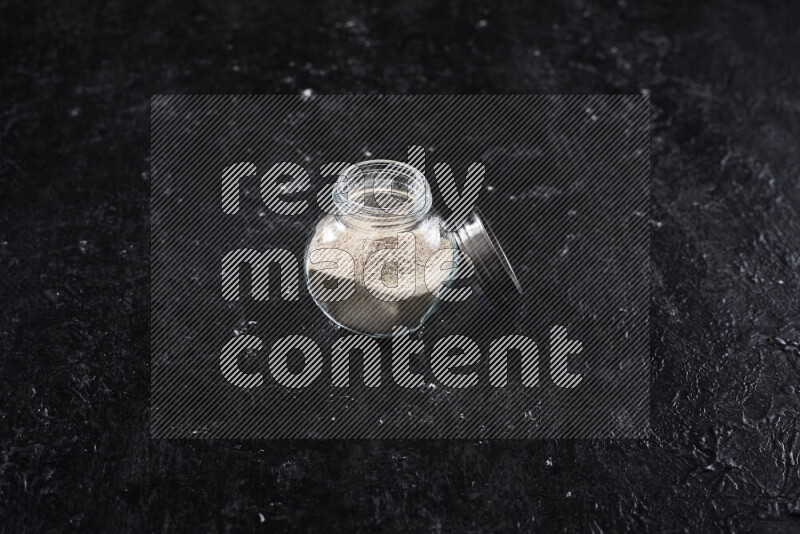 A glass jar full of onion powder on black background