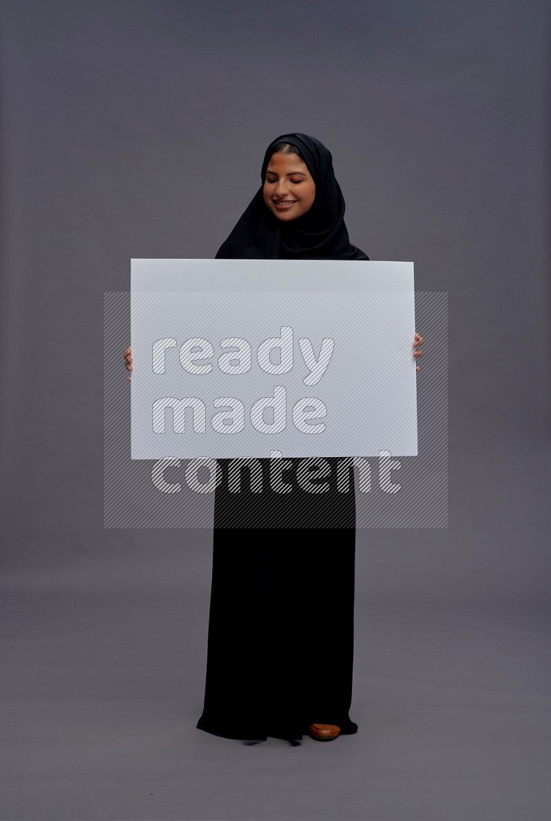 Saudi woman wearing Abaya standing holding white board on gray background