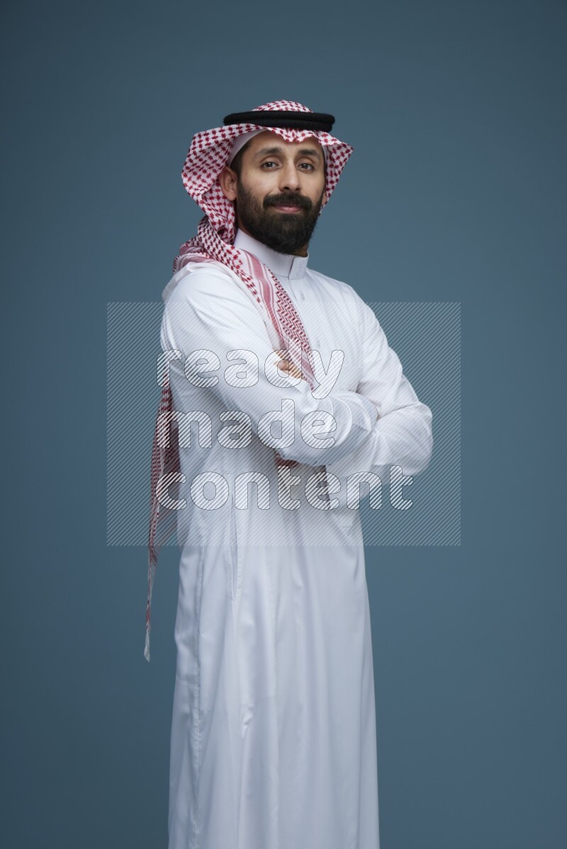 A man posing in a blue background wearing Saudi Thob and Shomag