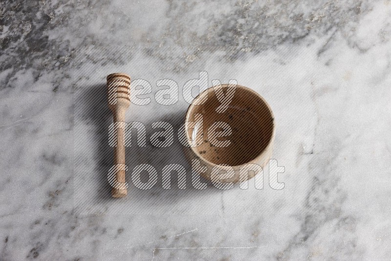 Multicolored Pottery bowl with wooden honey handle on the side with grey marble flooring, 65 degree angle