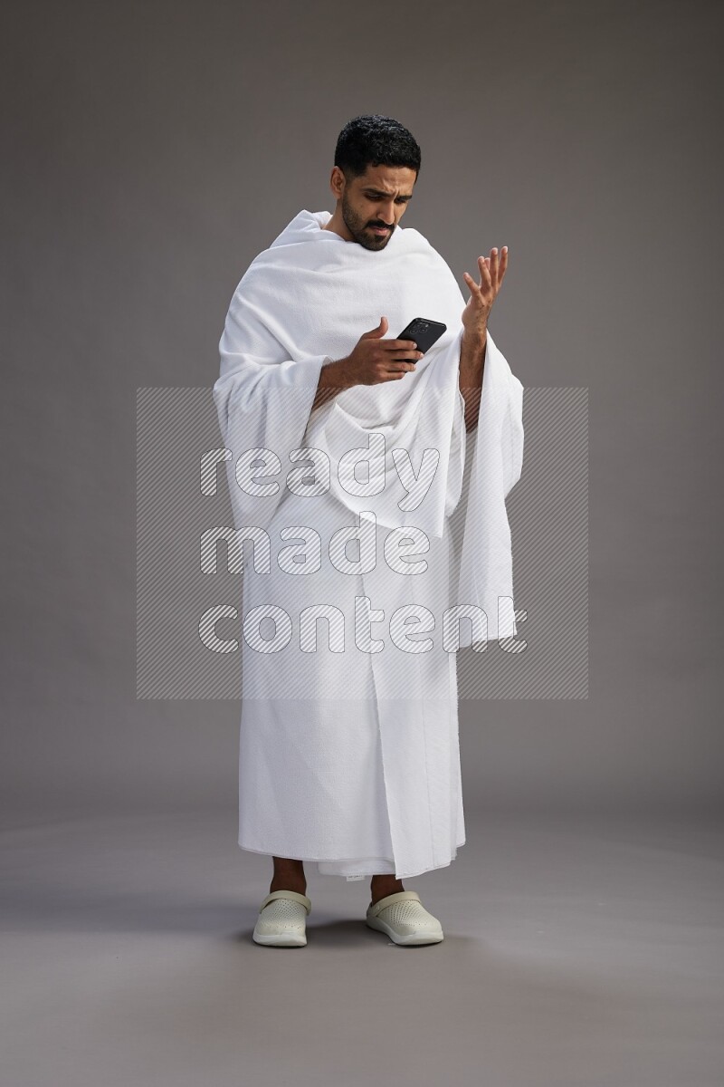 A man wearing Ehram Standing texting on phone on gray background