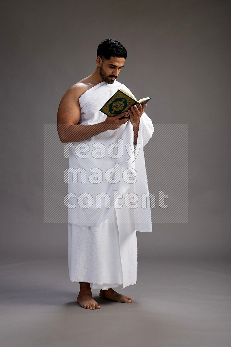 A man wearing Ehram Standing reading quran on gray background