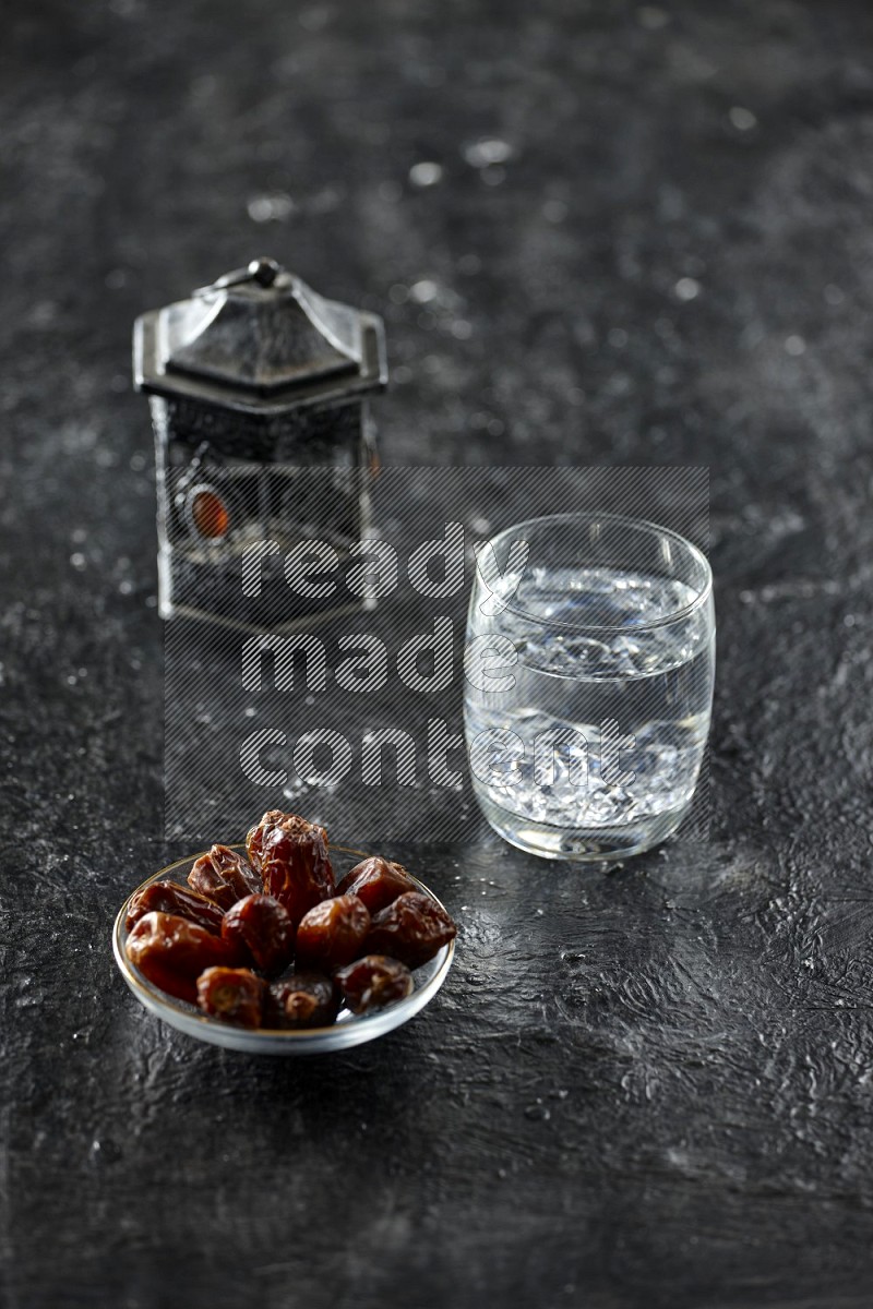 A silver lantern with drinks, dates, nuts, prayer beads and quran on textured black background