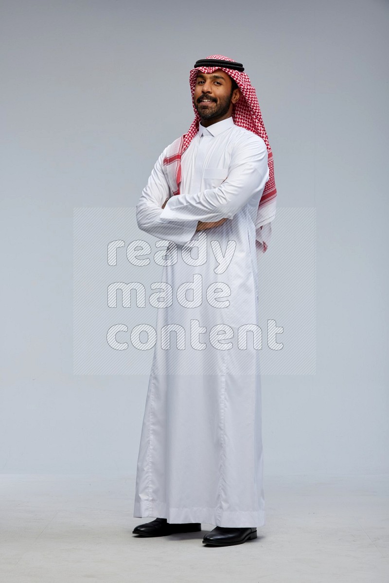 Saudi man Wearing Thob and shomag standing with crossed arms on Gray background