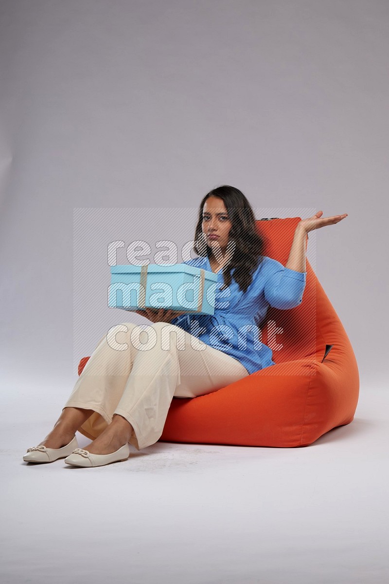 A woman sitting on an orange beanbag and opining a gift