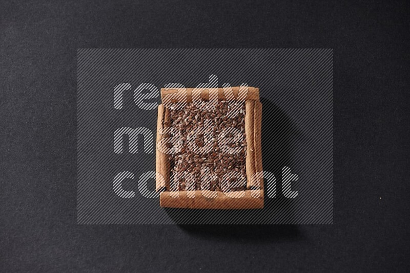 A single square of cinnamon sticks full of flaxseeds on black flooring