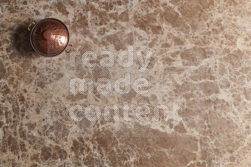 A small copper pot on beige marble background