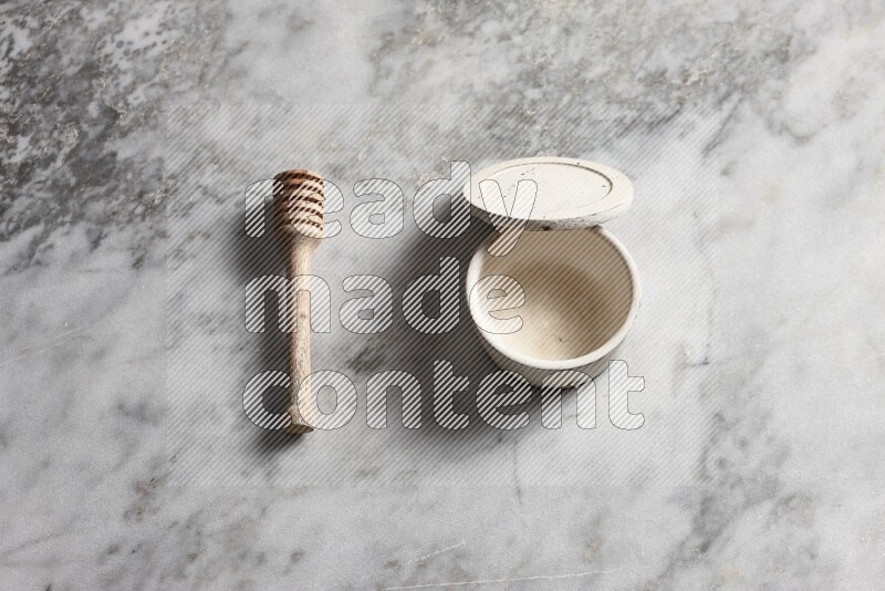 White pottery bowl with wooden honey dipper on the side on grey marble background