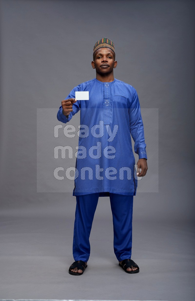 Man wearing Nigerian outfit standing holding ATM card on gray background