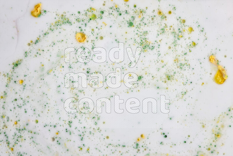 The image captures a splatter of yellow and green paint over a white backdrop