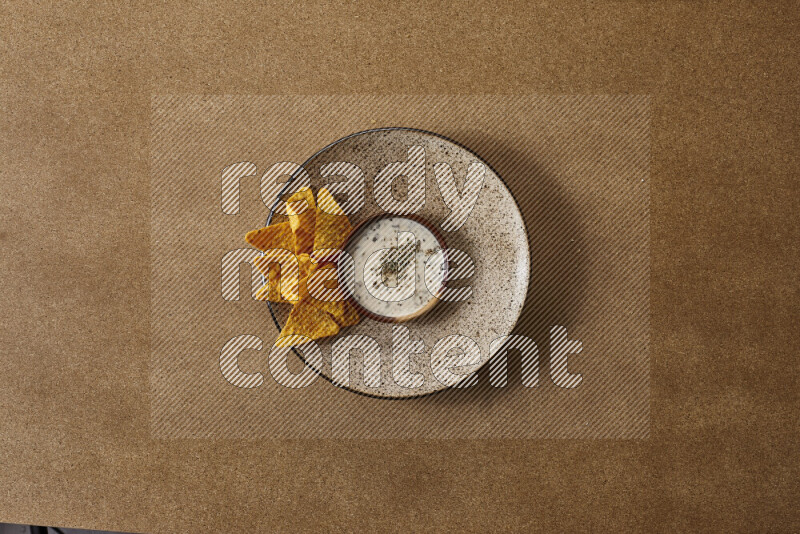 Assorted snacks on a pottery plate with a dipping on brown background