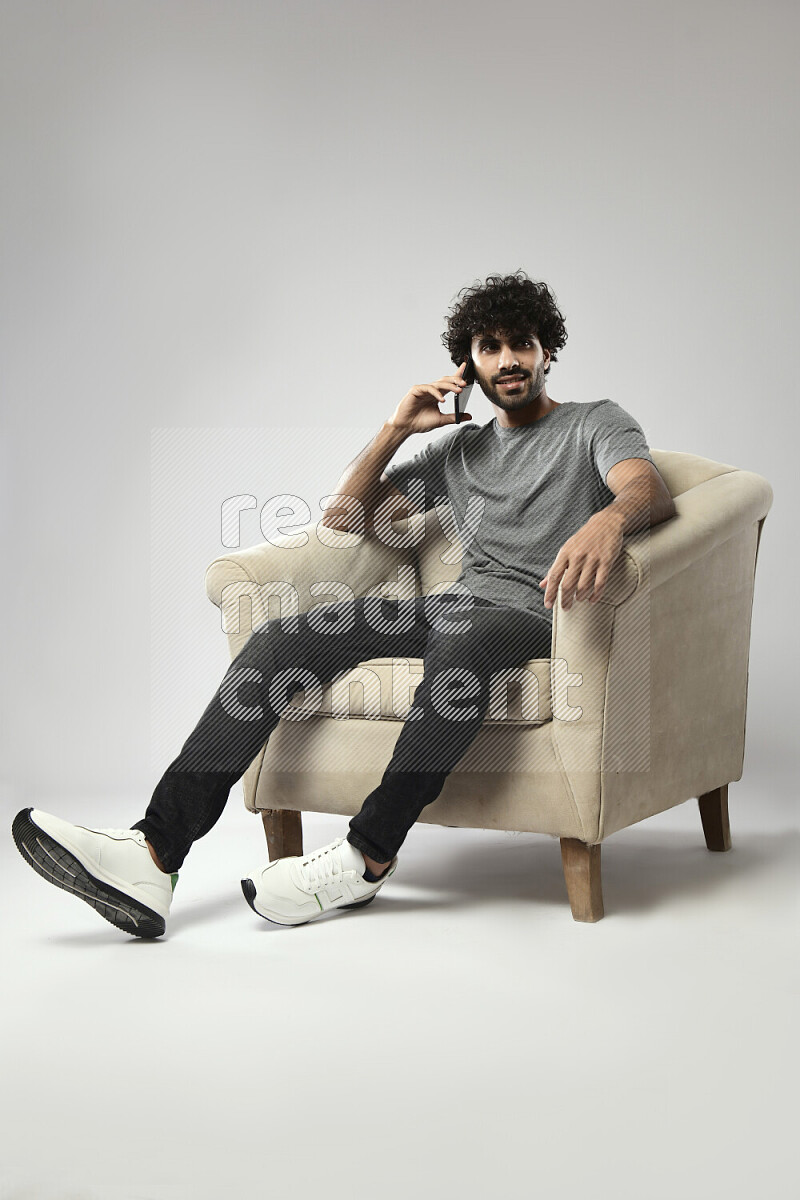 A man wearing casual sitting on a chair talking on the phone on white background