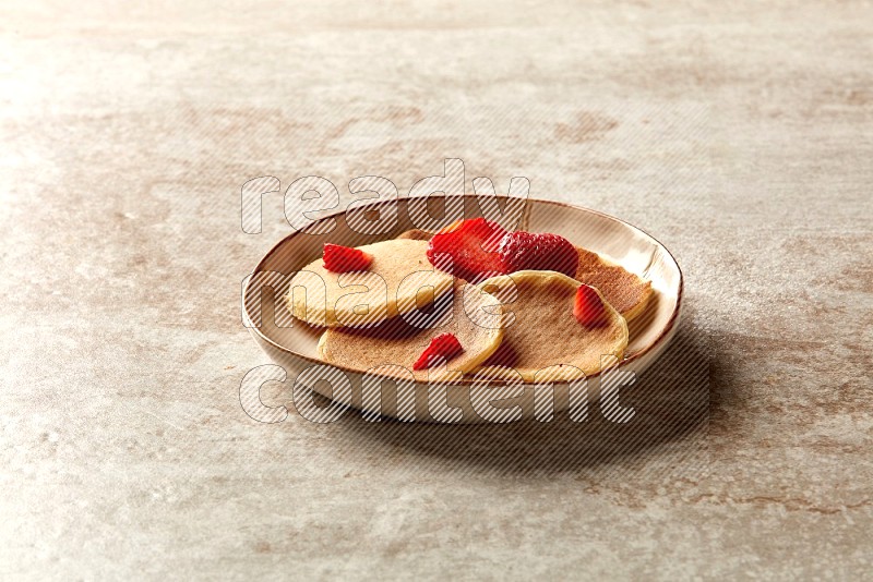 Five stacked strawberry mini pancakes in an irregular plate on beige background