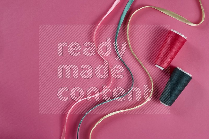 A green and pink collection of sewing and tailoring tools arranged on a pink background