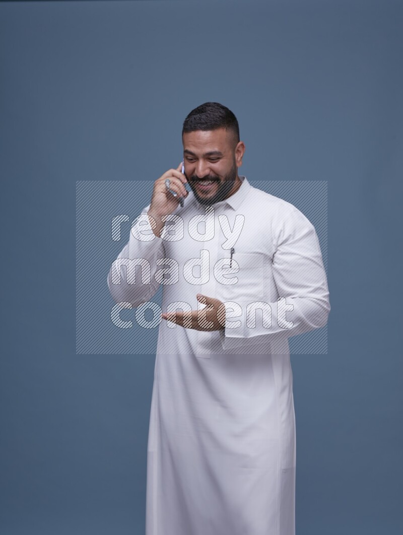 A Saudi man calling on blue background wearing Saudi Thob