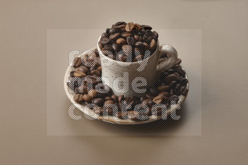 A beige pottery cup full of roasted coffee beans on beige background