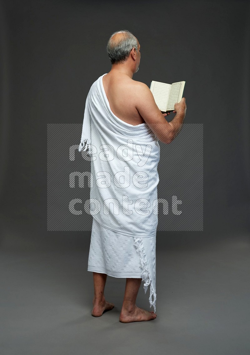 A man wearing Ehram Standing reading quran on gray background