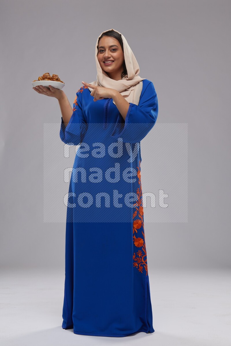 A Saudi woman standing wearing Jalabeya holding a plate of dates