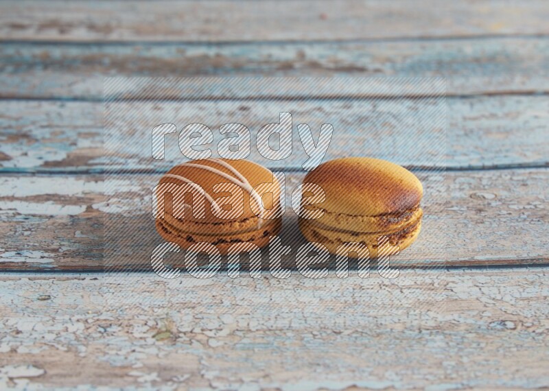 45º Shot of of two assorted Brown Irish Cream, and Yellow Crème Brulée macarons on light blue background