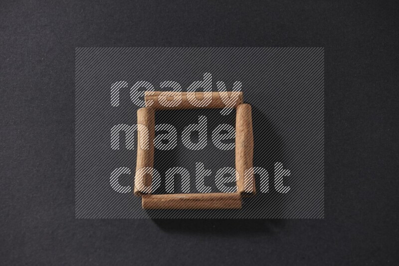 A single square of cinnamon sticks on black flooring