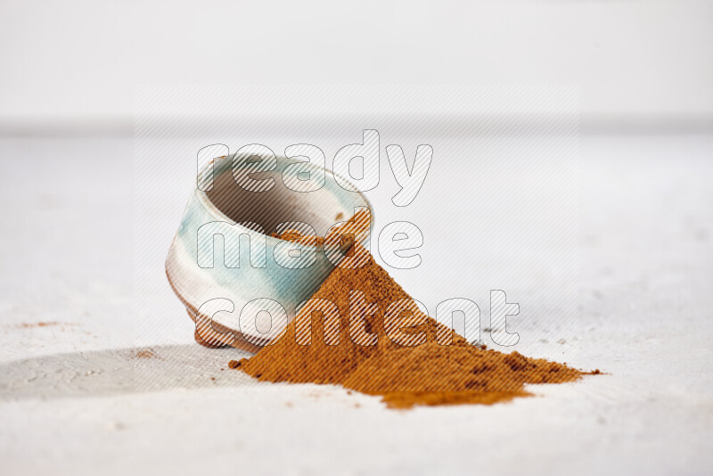 A colored pottery bowl full of ground paprika powder with fallen powder from it on white background