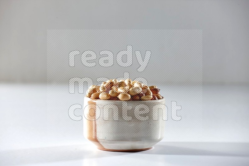 A beige ceramic bowl full of peeled peanuts on a white background in different angles