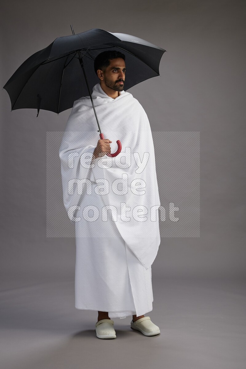 A man wearing Ehram Standing holding umbrella on gray background