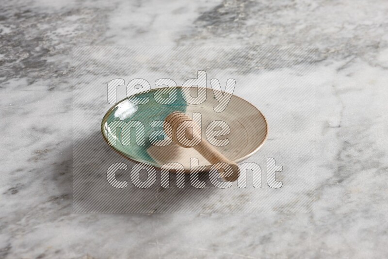 Multicolored pottery plate with wooden honey dipper in it on grey marble background