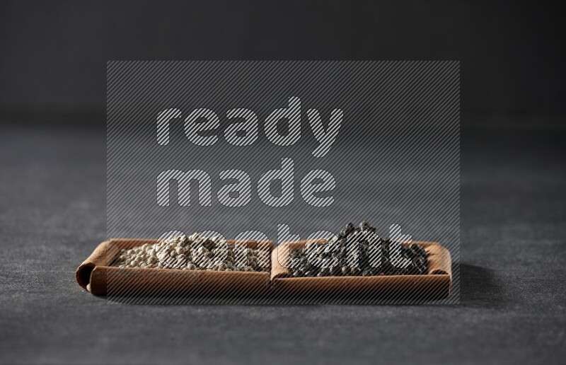 مربعان من أعواد القرفة ممتلئان بحبوب الفلفل الأبيض وحبوب الفلفل الأسود علي خلفية سوداء