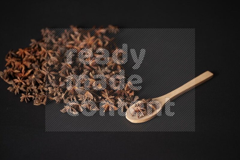 اليانسون النجمي في ملعقة خشبية ومتناثر على أرضية سوداء