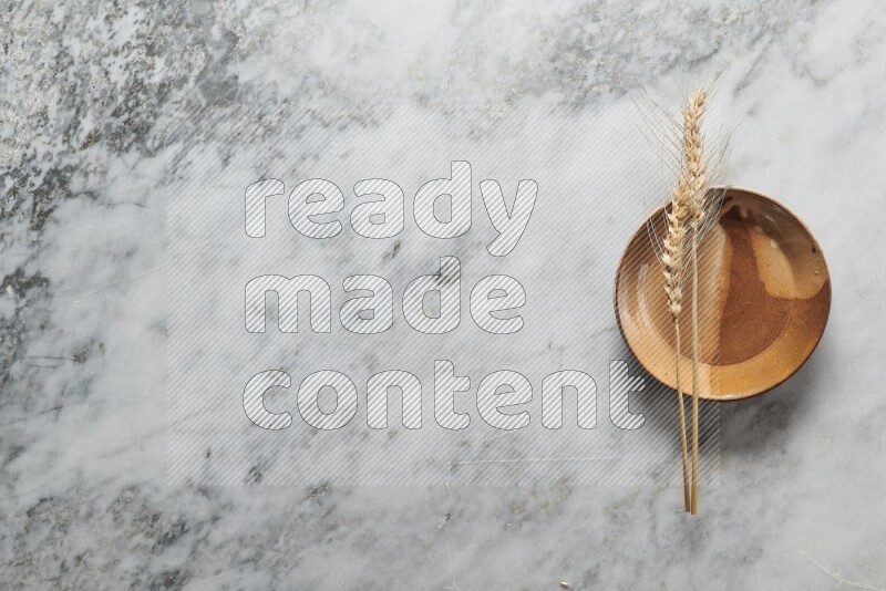 Wheat stalks on multicolored pottery plate on grey marble background