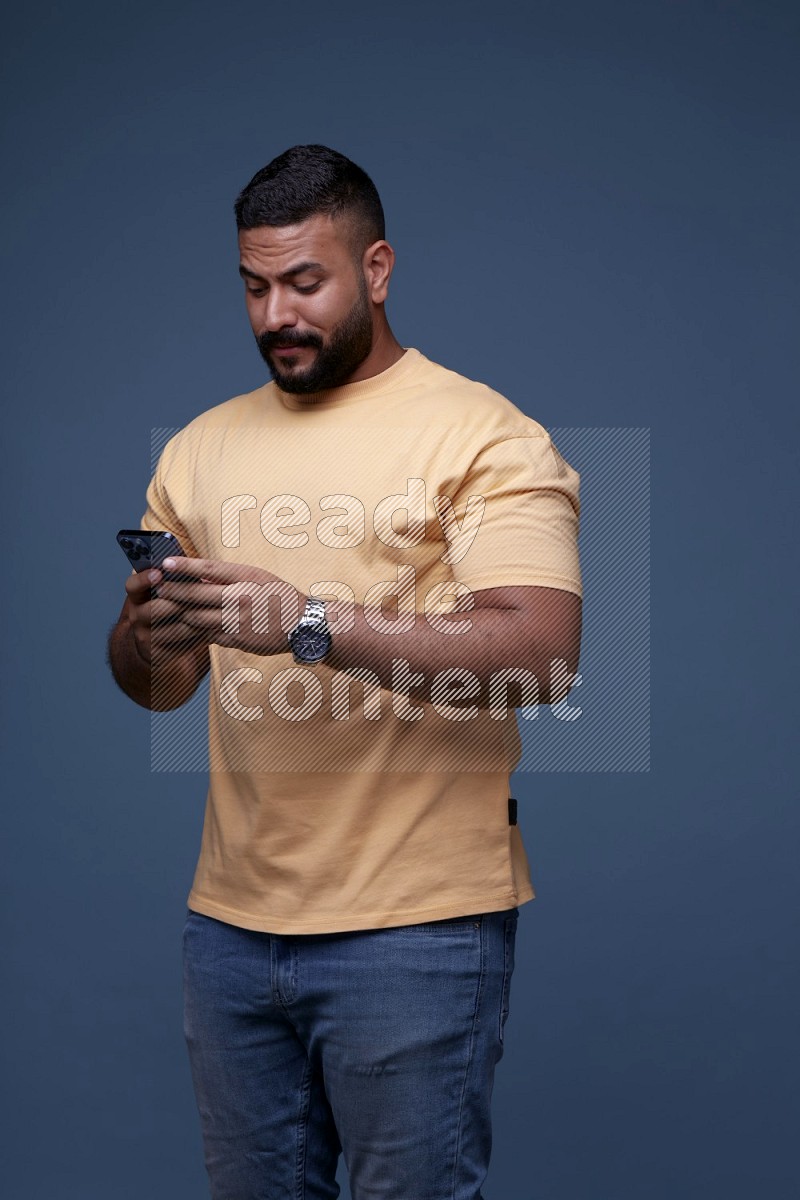 رجل يرتدي قميص اصفر وبنطال جينز ازرق يستخدم جواله
