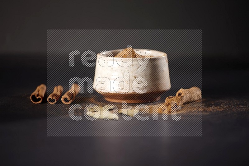 Cinnamon powder in a white pottery bowl and cinnamon sticks and laurel leaves on black background