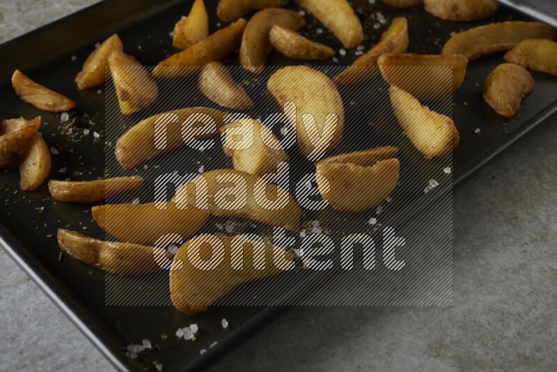 wedges potato in a black stainless steel rectangle tray on grey textured counter top